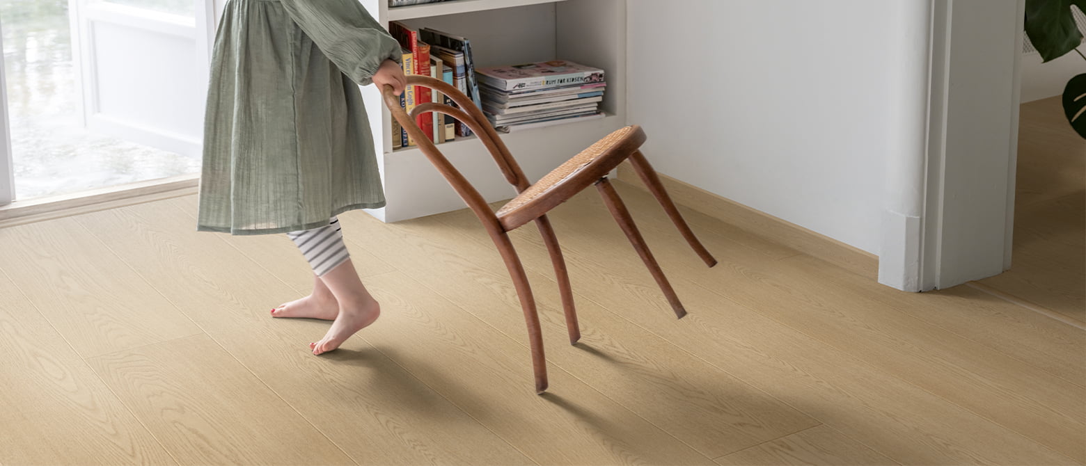 little girl dragging chair on beige laminate floor